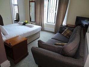 A hotel room with a bed, a sofa, a TV, and a window with curtains.