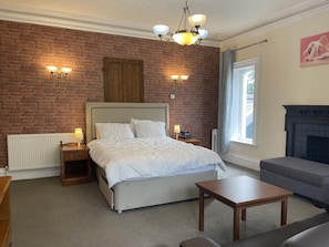 A bedroom with a brick wall, a bed, bedside lamps, a fireplace, and a window.
