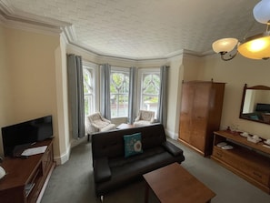 A living room with a black sofa, two patterned armchairs, a wooden cabinet, and a television on a wooden stand. - Milverton Hotel by Bevolve - Free Parking (Manchester)
