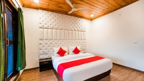 A bedroom with a tufted headboard, a bed with a red and white bedspread, a wooden floor, and a ceiling fan. - Goroomgo Blue Moon Bhimtal (Nainital)