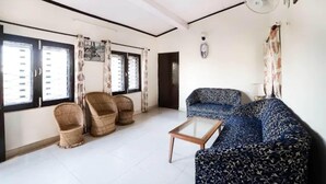 A living room with a sofa, two armchairs, a coffee table, and a ceiling fan. - Goroomgo Blue Moon Bhimtal (Nainital)
