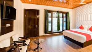 A hotel room with a bed, a TV, a desk, and a window with curtains.