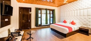 A hotel room with a bed, a TV, a desk, and a window with curtains.