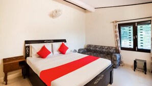 A bedroom with a bed, a sofa, a bedside table, a window, and a wall-mounted light fixture. - Goroomgo Blue Moon Bhimtal (Nainital)