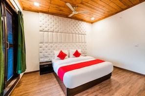 A bedroom with a tufted headboard, a bed with a red and white bedspread, a wooden floor, and a ceiling fan.