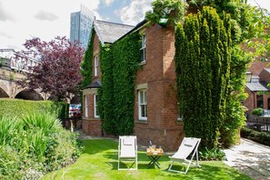 A brick building with ivy-covered walls, a grassy lawn, and two white lounge chairs.
