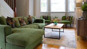 A living room with a green sofa, two armchairs, a coffee table, and a staircase.