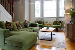 A living room with a green sofa, two armchairs, a coffee table, and a staircase.