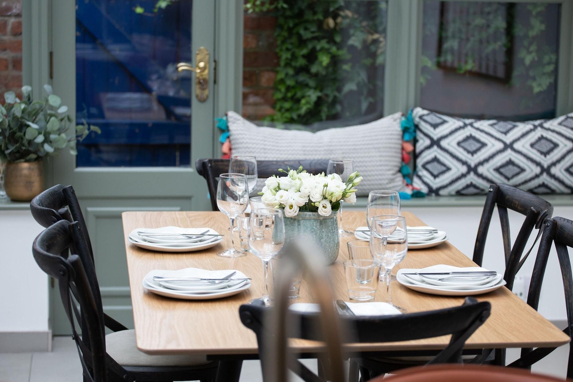 A dining table set with plates, cutlery, and glasses, with a vase of flowers in the center.