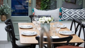 Une table à manger dressée avec des assiettes, des couverts et des verres, et un vase rempli de fleurs placé au centre.