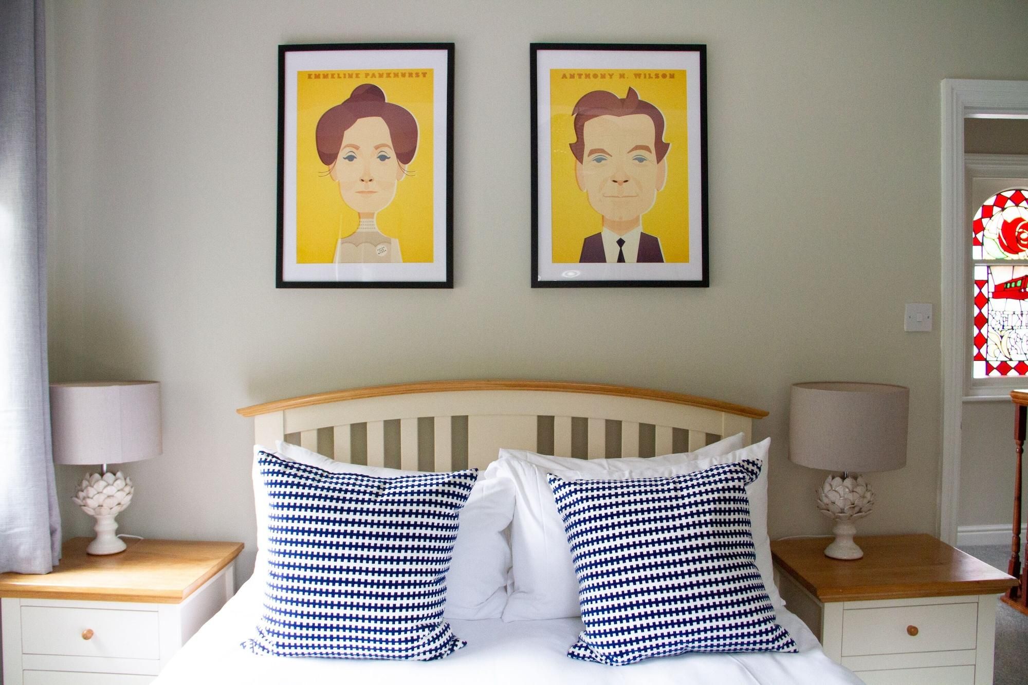 A bedroom with a bed, two nightstands, two lamps, and two framed portraits on the wall.