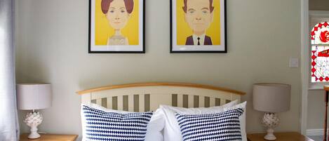 Un dormitorio con una cama, dos mesitas de noche, dos lámparas y dos retratos enmarcados en la pared.
