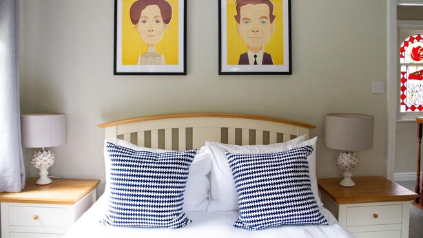 Une chambre à coucher comprenant un lit, deux tables de chevet, deux lampes et deux portraits encadrés accrochés au mur.