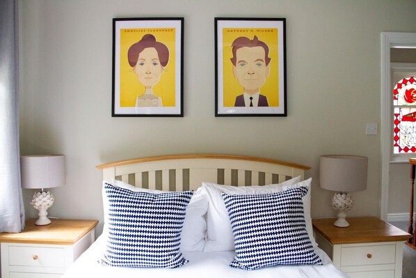 A bedroom with a bed, two nightstands, two lamps, and two framed portraits on the wall.