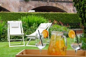 A garden setting with a tray of drinks and two white lounge chairs.