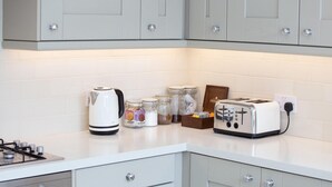 Une cuisine équipée d’une cuisinière à gaz, d’une bouilloire blanche, d’un grille-pain et de pots d’épices disposés sur le plan de travail.