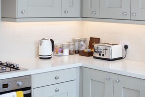 A kitchen with a gas stove, a white kettle, a toaster, and jars of spices on the counter.