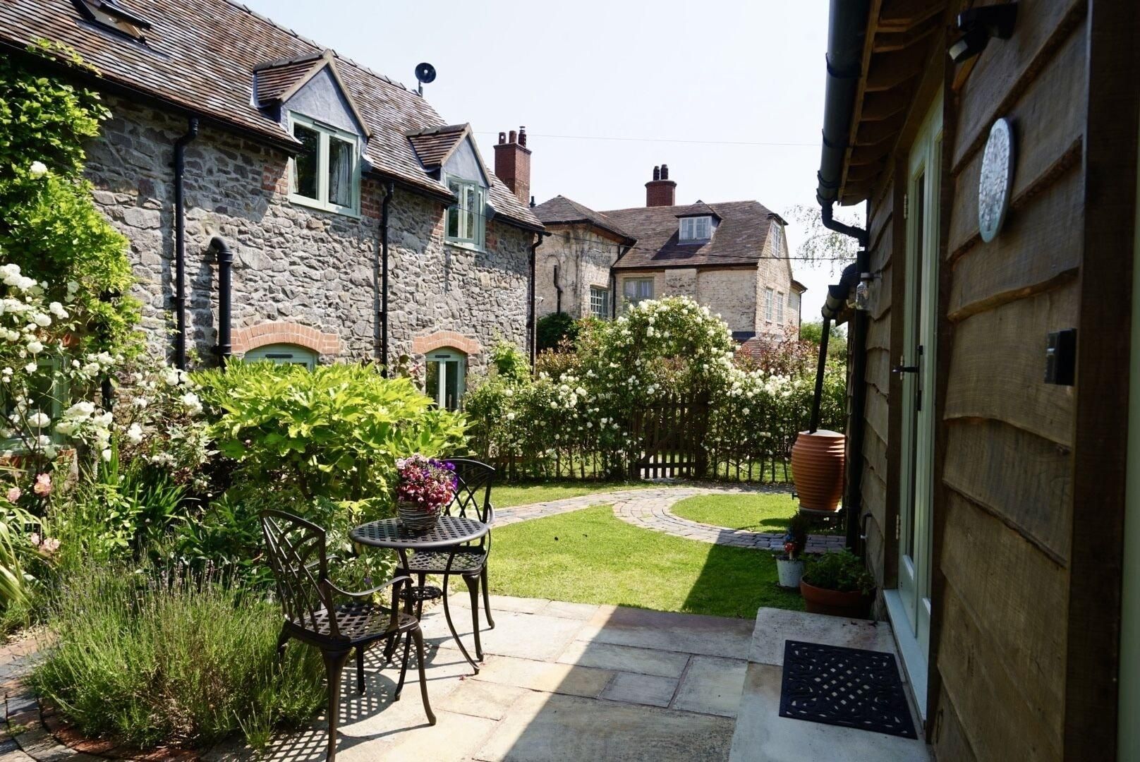 Une maison en pierre avec un patio et un jardin, une petite table et des chaises.