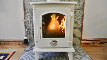 A white wood-burning stove with a glass door, a metal handle, and a circular dial.