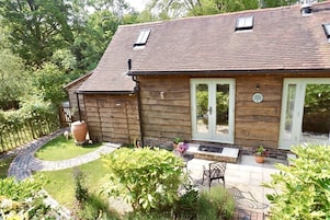 Una casa de madera con techo inclinado, un patio cercado y un patio empedrado con mobiliario exterior.