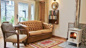 A cozy living room with a leather sofa, a wooden chair, a bookshelf, a fireplace, and a patterned rug.