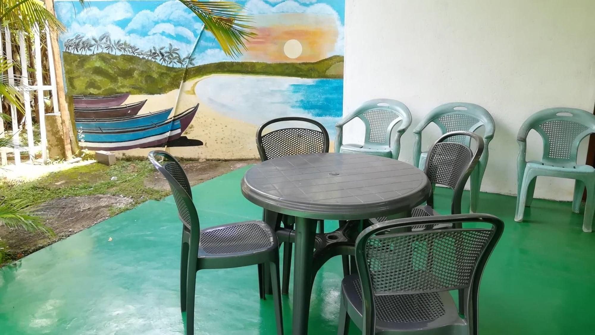 An outdoor seating area with a round table and chairs, a mural of a beach scene, and a small pool.