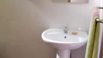 A bathroom with a white sink, a mirror, and a green storage basket.