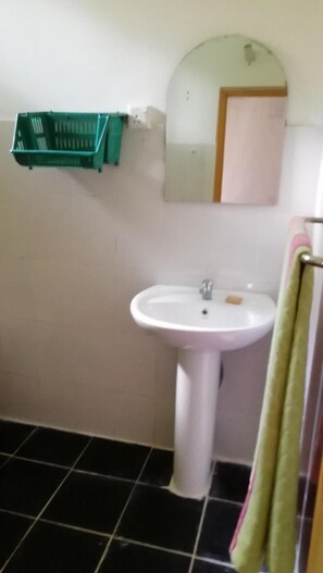 Un baño con un lavamanos blanco, un espejo y una cesta de almacenamiento verde.