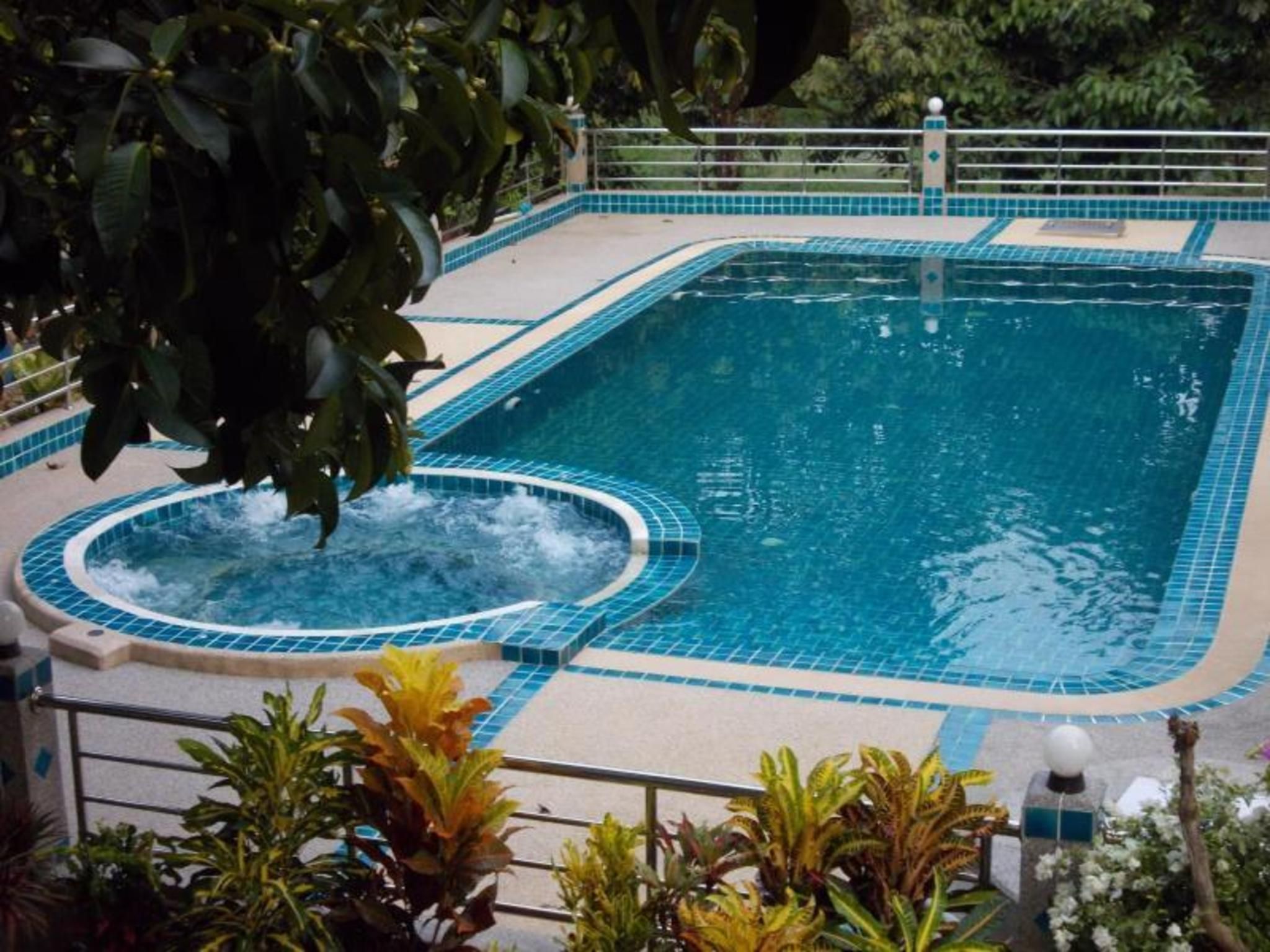 Une piscine rectangulaire avec un jacuzzi au centre, entourée d’une terrasse carrelée et bordée d’une rambarde en métal.