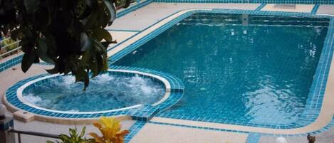 Une piscine rectangulaire avec un jacuzzi au centre, entourée d’une terrasse carrelée et bordée d’une rambarde en métal.