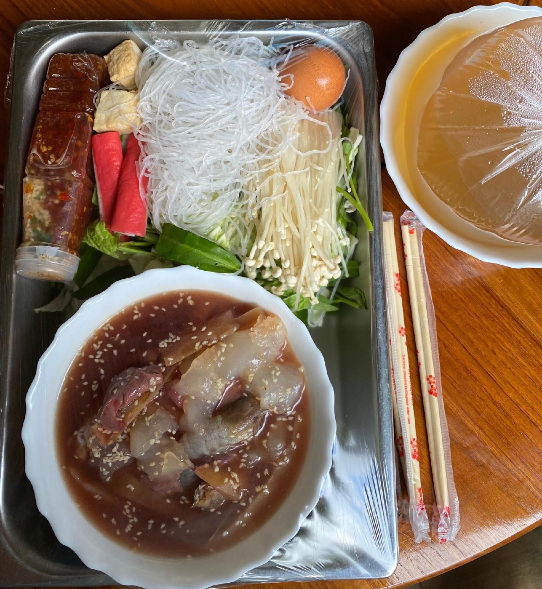 Bandeja de comida con diferentes alimentos, como fideos, verduras y un tazón de sopa.