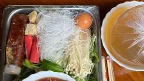 Un vassoio con diversi cibi, tra cui noodles, verdure e una ciotola di zuppa.