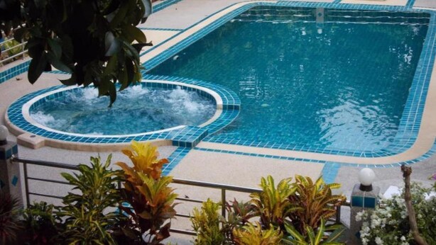 Una piscina rettangolare con una vasca idromassaggio al centro, circondata da un solarium piastrellato e delimitata da una ringhiera in metallo.
