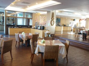 Un restaurant amb diverses taules i caires, una zona de cuina i una barra.