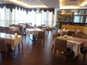 A restaurant with multiple tables and chairs, a wooden floor, and a view of the outside through large windows. - East Coast Sea View Hotel (Chenggong)