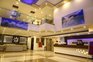 A hotel lobby with a reception desk, a seating area with a sofa, and a large painting on the wall. - The Pearl Grand Hotel (Dehradun)