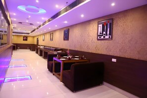 A hotel lobby with a long reception desk, seating area, and a wall with framed artwork. - The Pearl Grand Hotel (Dehradun)