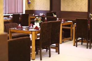 A restaurant interior with wooden tables and chairs, a vase with flowers, and a menu stand. - The Pearl Grand Hotel (Dehradun)
