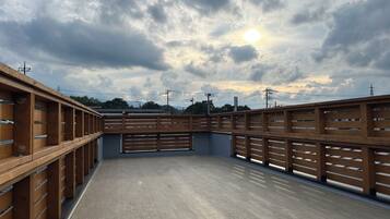 A covered outdoor area with a wooden fence and a concrete floor, under a cloudy sky with the sun visible.