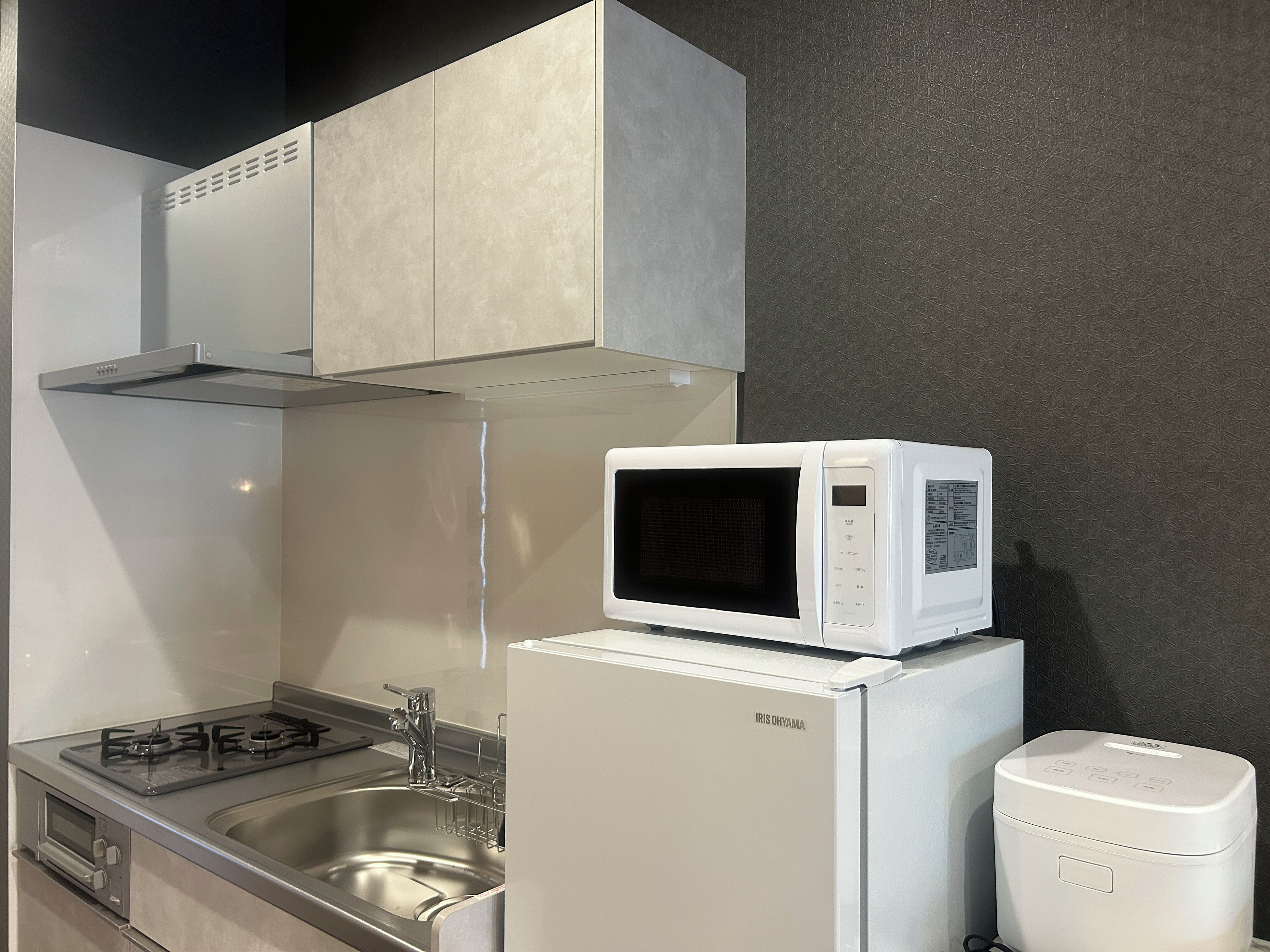 A compact kitchen with a microwave on top of a white refrigerator, a stainless steel sink, and a gas stove.