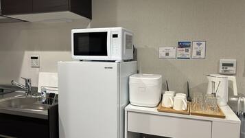 A kitchen with a microwave, refrigerator, coffee maker, and a tray with glasses and a coffee pot.
