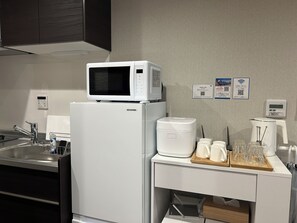 A kitchen with a microwave, refrigerator, coffee maker, and a tray with glasses and a coffee pot.