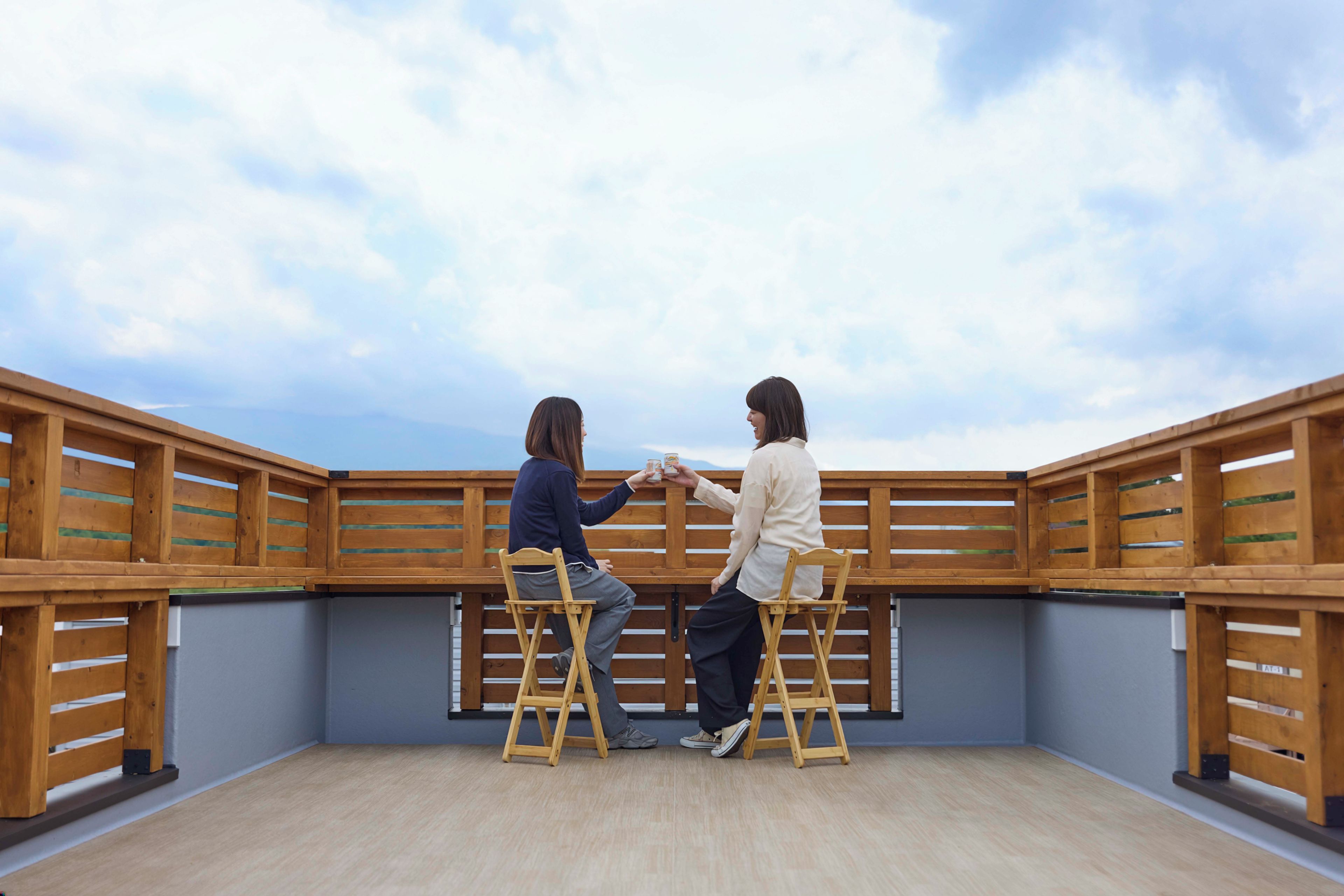 Two individuals on wooden ladders in a room with a view of the sky.