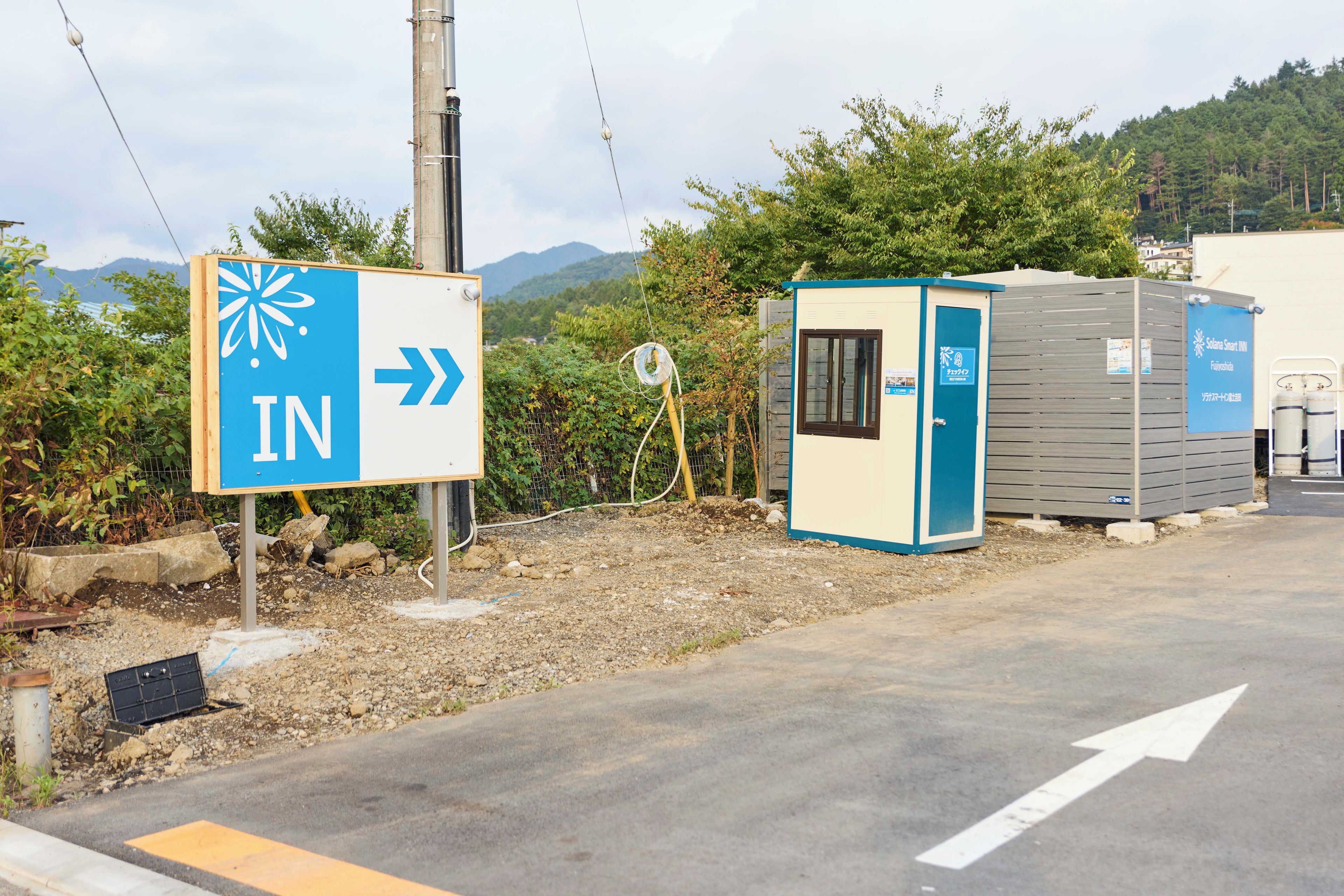 A directional sign with an arrow pointing to the right, a portable toilet, and a utility box with a solar panel.