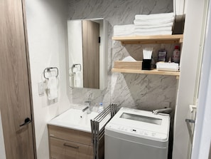 Un baño moderno con pared de mármol, un lavamanos, un espejo, un perchero para toallas, un estante con artículos de aseo y una lavadora.