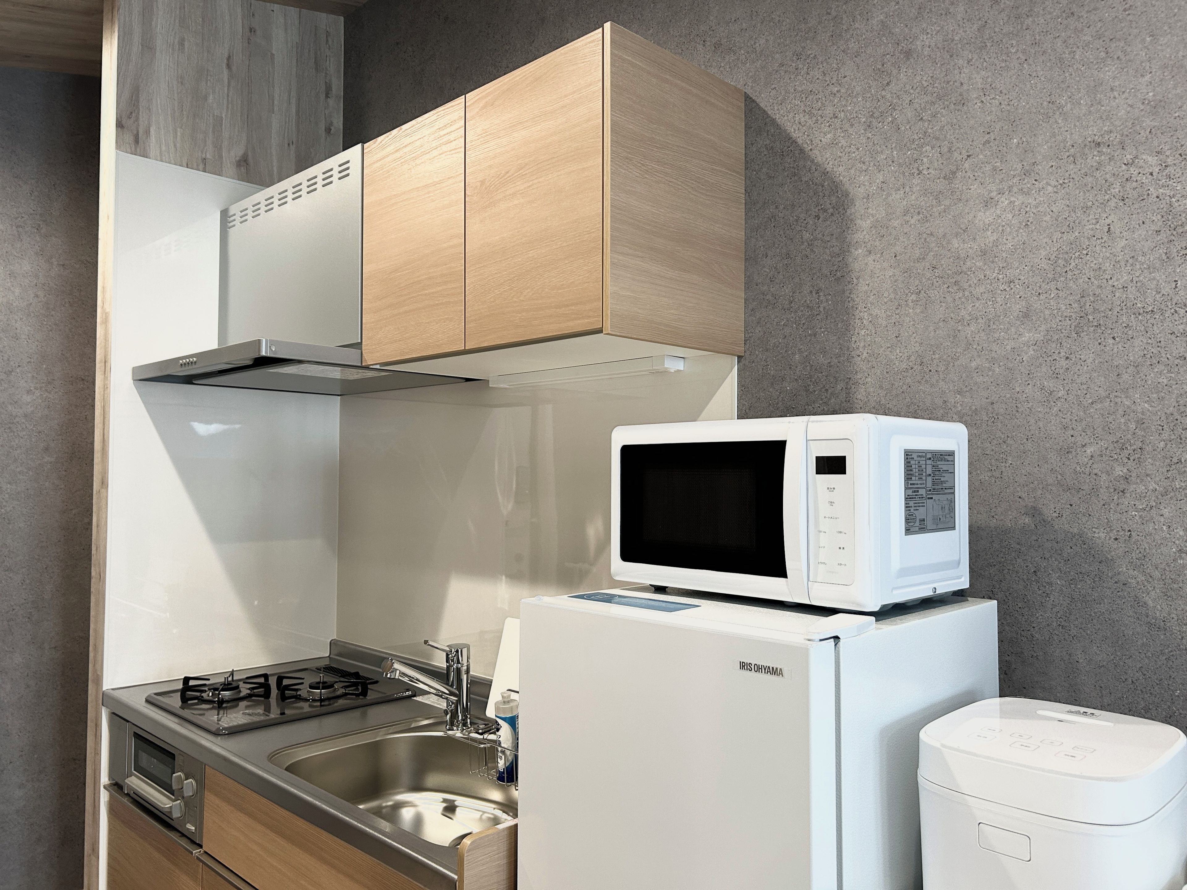 A compact kitchen with a microwave on top of a refrigerator, a gas stove, and wooden cabinets.