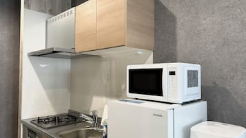 A compact kitchen with a microwave on top of a refrigerator, a gas stove, and wooden cabinets.