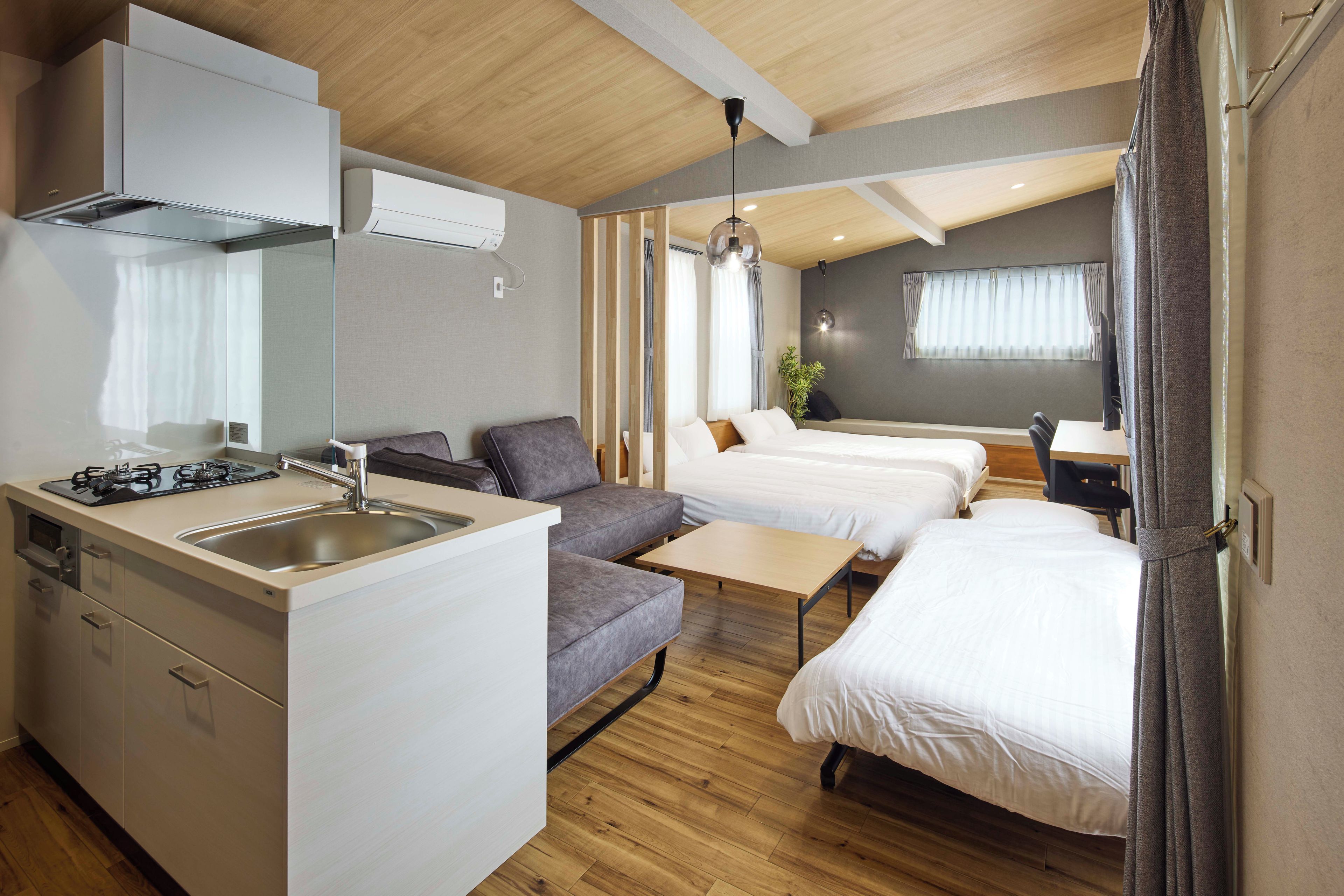 A compact hotel room with a kitchenette, two beds, a sofa, and a dining table.