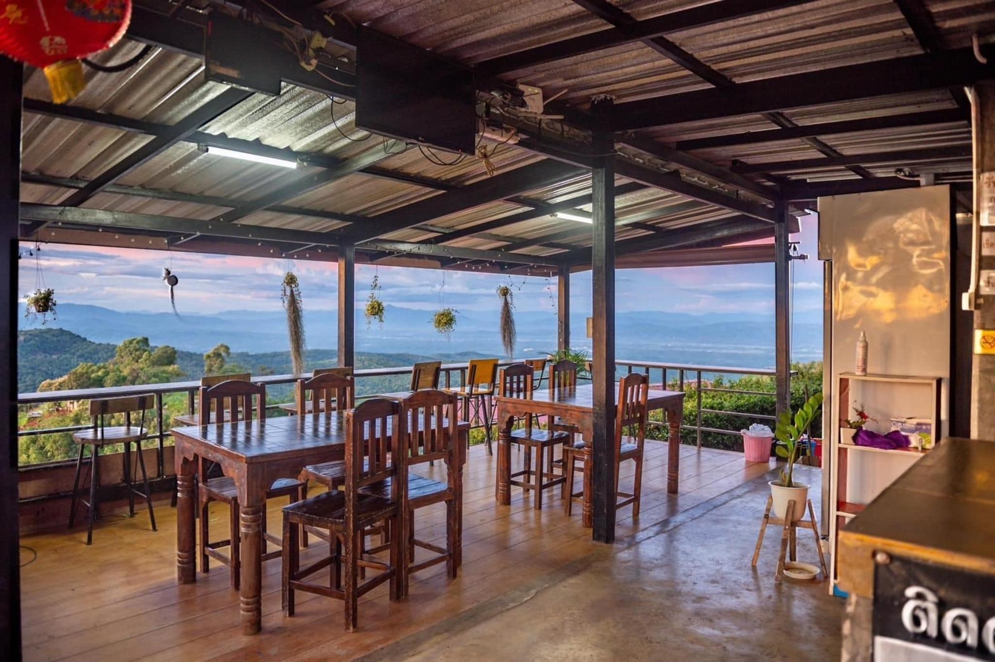 An outdoor dining area with wooden tables and chairs, overlooking a mountainous landscape.