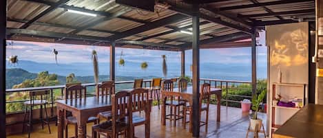 An outdoor dining area with wooden tables and chairs, overlooking a mountainous landscape.